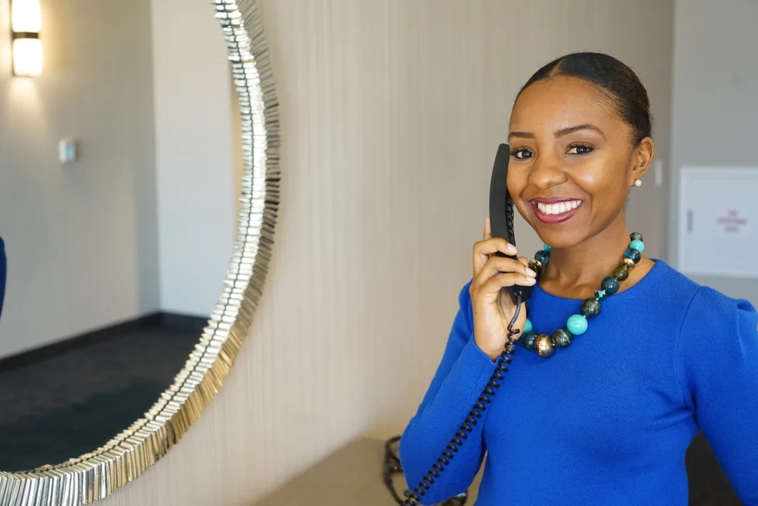 Shauntelle Senkungu smiling as she takes a call on the desk phone at the WelcomeMed front office.